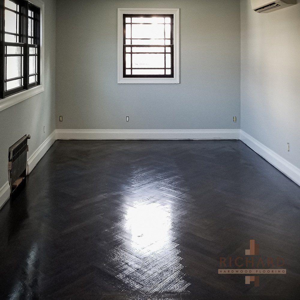An empty room with pale gray walls, white trim, and dark, glossy herringbone wood floors.