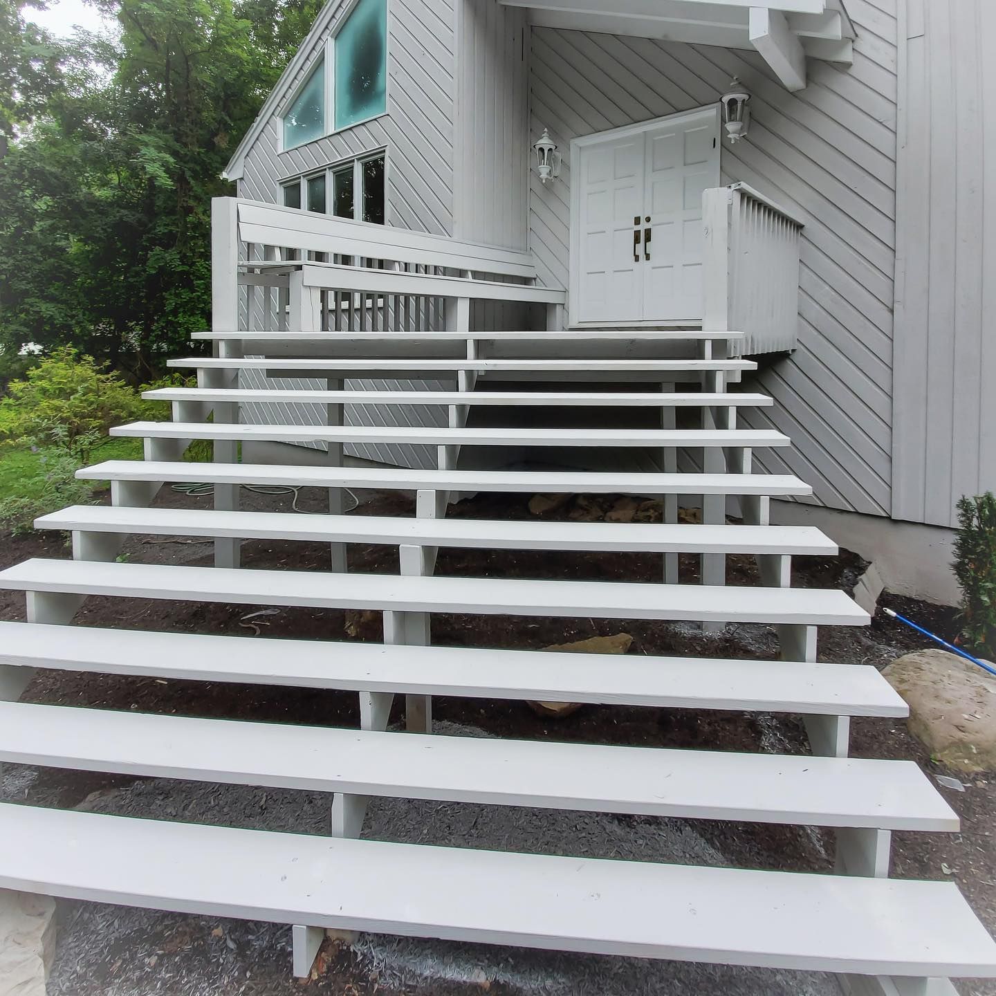 A long, wide set of painted white wooden stairs leads up to the front entrance of a grey, modern-style house.