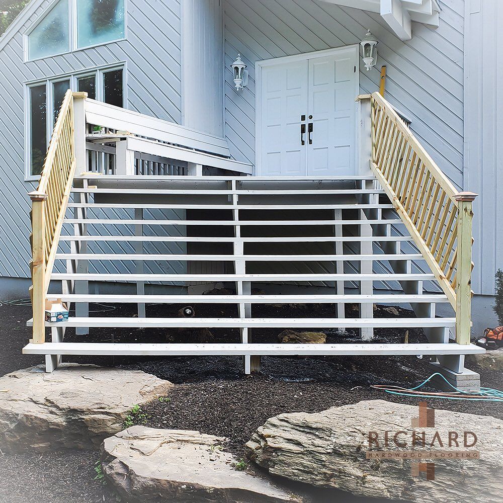 Wide white wooden stairs with lattice railings lead up to a white double-door entrance on a grey-sided house.