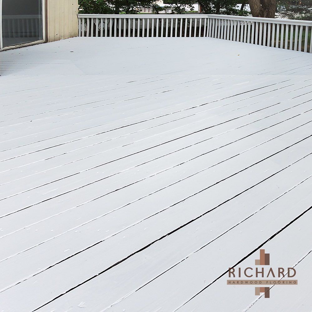 A freshly painted white wooden deck with white railings, featuring a small Richard Hardwood Flooring logo in the corner.