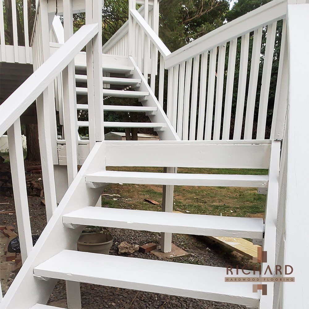 A set of outdoor wooden stairs painted white, featuring matching railings, leading up to an elevated deck or porch.