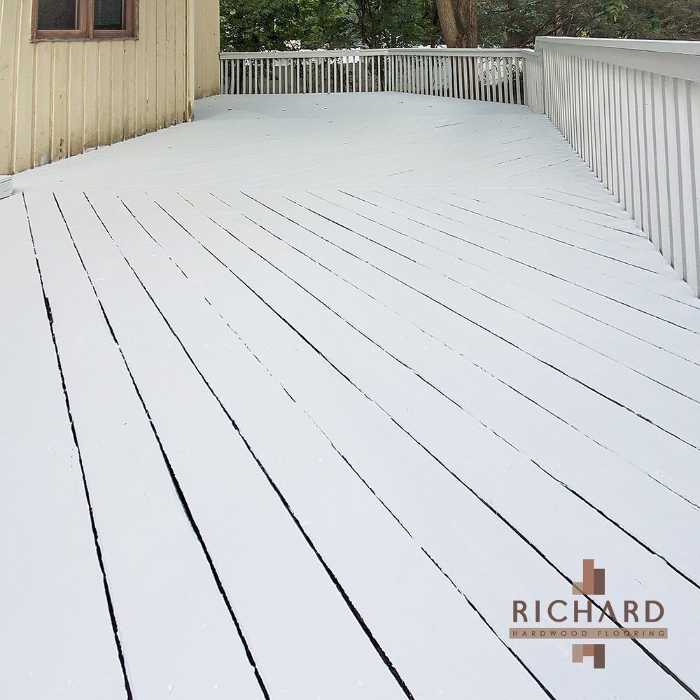 A white-painted wooden deck with diagonal planks attached to a tan building, featuring white railings.