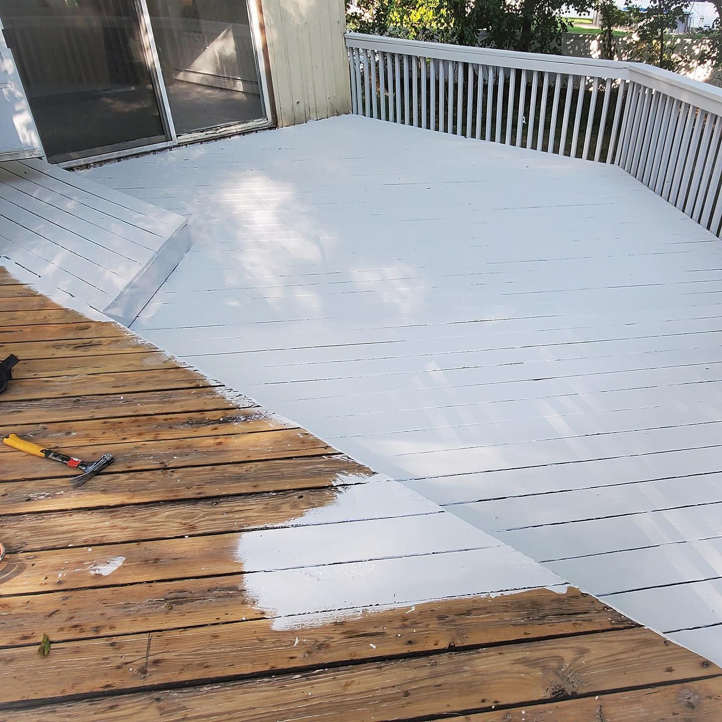 A wooden deck in the process of being painted, with one half finished in white paint and the other showing raw wood.