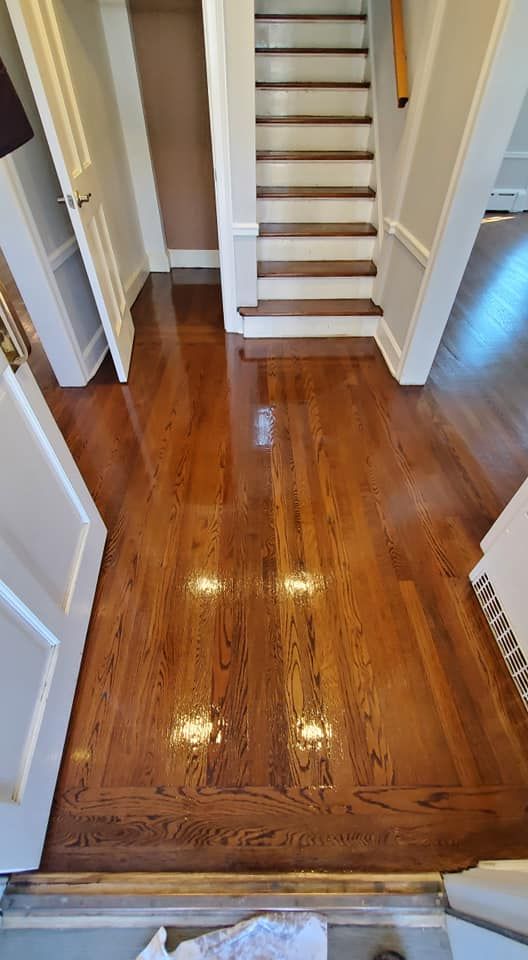 A polished, honey-colored hardwood floor leading to a staircase with white risers and brown treads in a bright hallway.