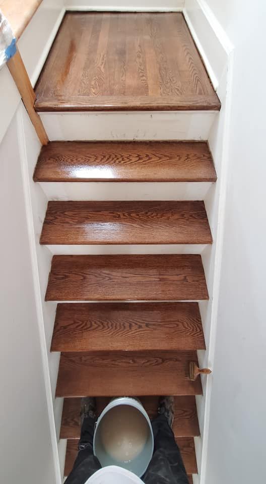 A first-person view looking down a narrow wooden staircase toward a small, light-colored circular sink at the bottom.
