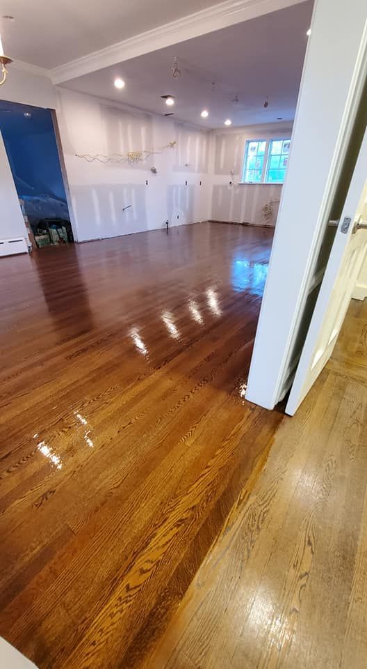 A view from a doorway into a room with freshly finished, glossy hardwood floors and white-painted walls.