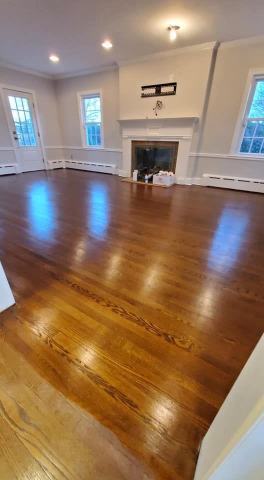 A spacious, empty room features gleaming dark wood floors, white walls, and a white fireplace mantel.