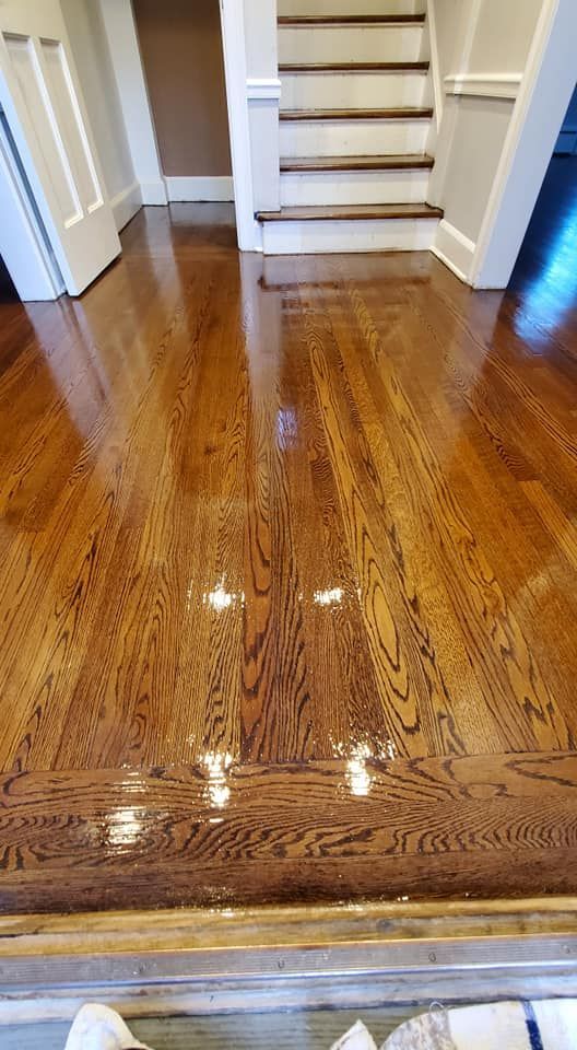 A high-angle view of a freshly finished, glossy hardwood floor with a dark stain, leading toward a white staircase.