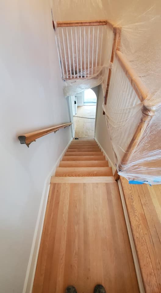 A downward view of wooden stairs leading to a doorway, with a handrail and plastic-covered railings under renovation.