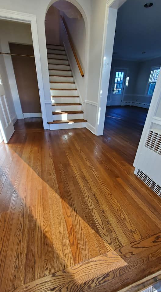 Polished hardwood floors lead to a staircase in an arched entryway, with a doorway revealing a sunlit room beyond.