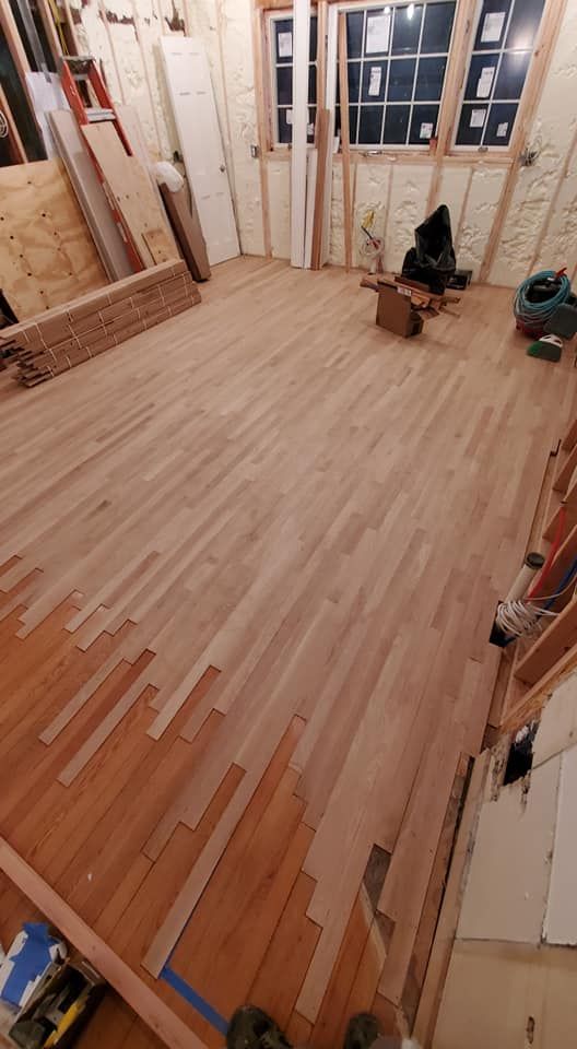 A room under renovation with new, light-toned wood flooring partially installed over a darker existing hardwood floor.