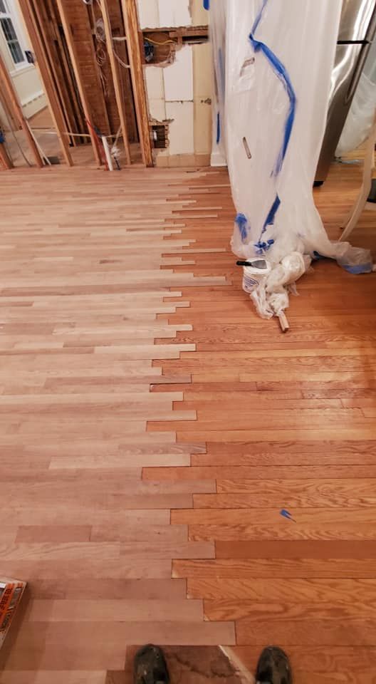 New, unfinished wood flooring is being woven into an existing, stained floor during a home renovation.