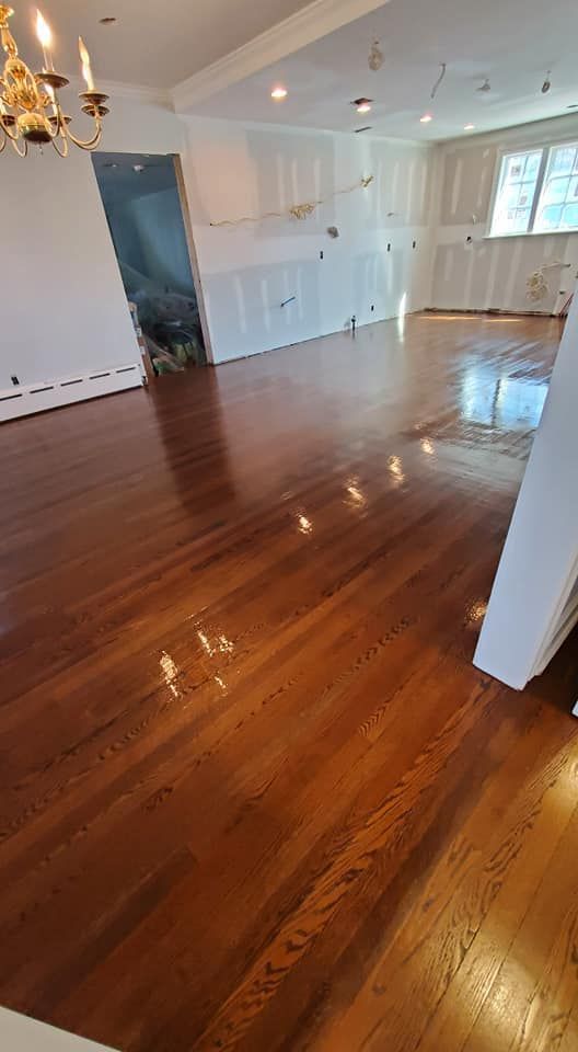 A renovated room featuring gleaming, polished hardwood floors, newly installed drywall, and a gold chandelier.