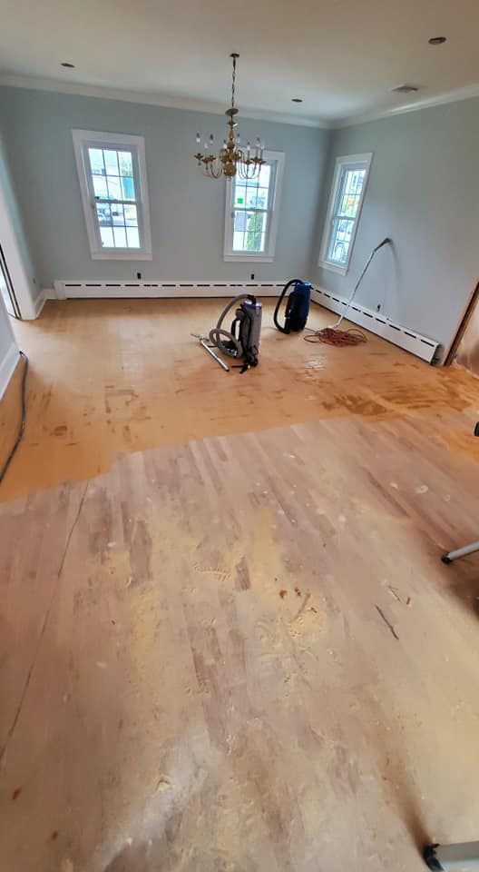 A dining room with light gray walls, a chandelier, and hardwood floors in the process of being sanded.