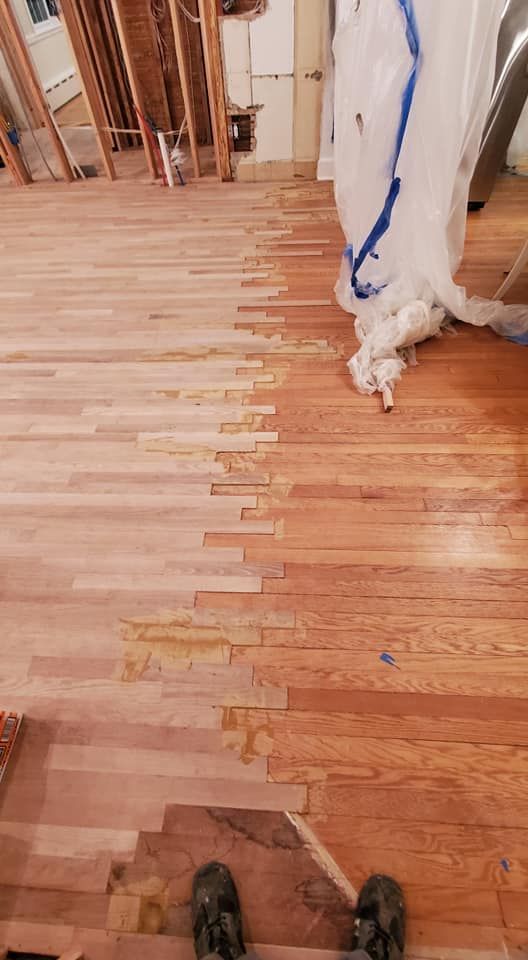 A view of a hardwood floor mid-refinishing, showing a transition between sanded, light wood and original, stained planks.