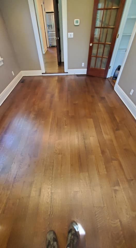 A perspective view of a room with polished wood flooring, leading to a doorway and a wooden-framed glass door.
