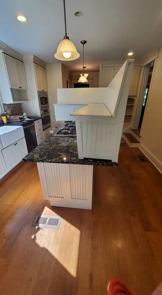 A white kitchen bench sits atop a granite kitchen island in a residential home with hardwood floors.