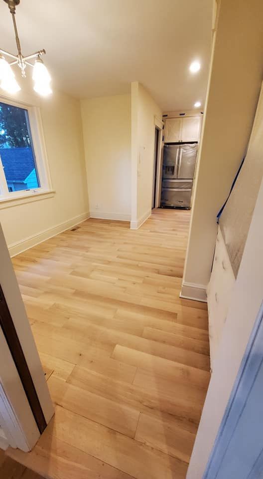 An interior view of a dining area with light hardwood floors, yellow walls, a hanging light fixture, and a distant fridge.