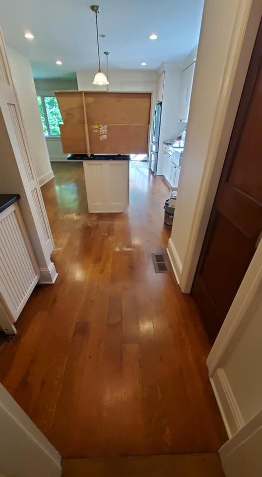 A large brown cardboard box sits on a white kitchen island in a brightly lit, wood-floored kitchen.