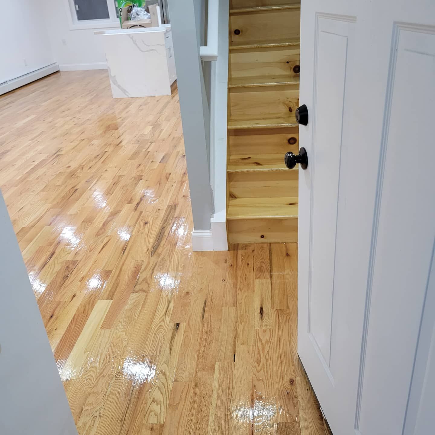 Interior view of a room with polished light wood floors, a wooden staircase, and an open white door.