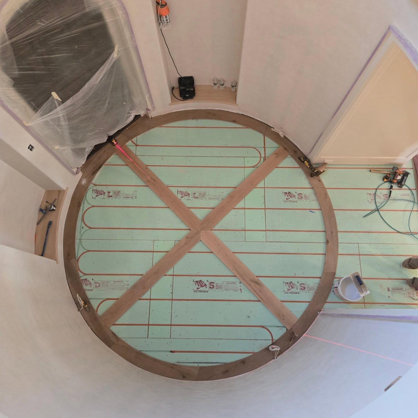 A top-down view of radiant floor heating coils installed on pale green insulation panels within a circular room frame.