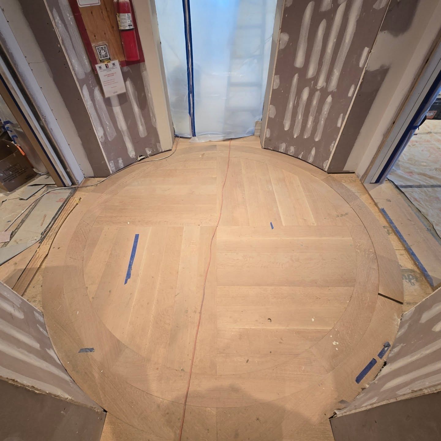 A circular wood floor inlay under construction in a doorway, surrounded by unfinished walls and flooring.