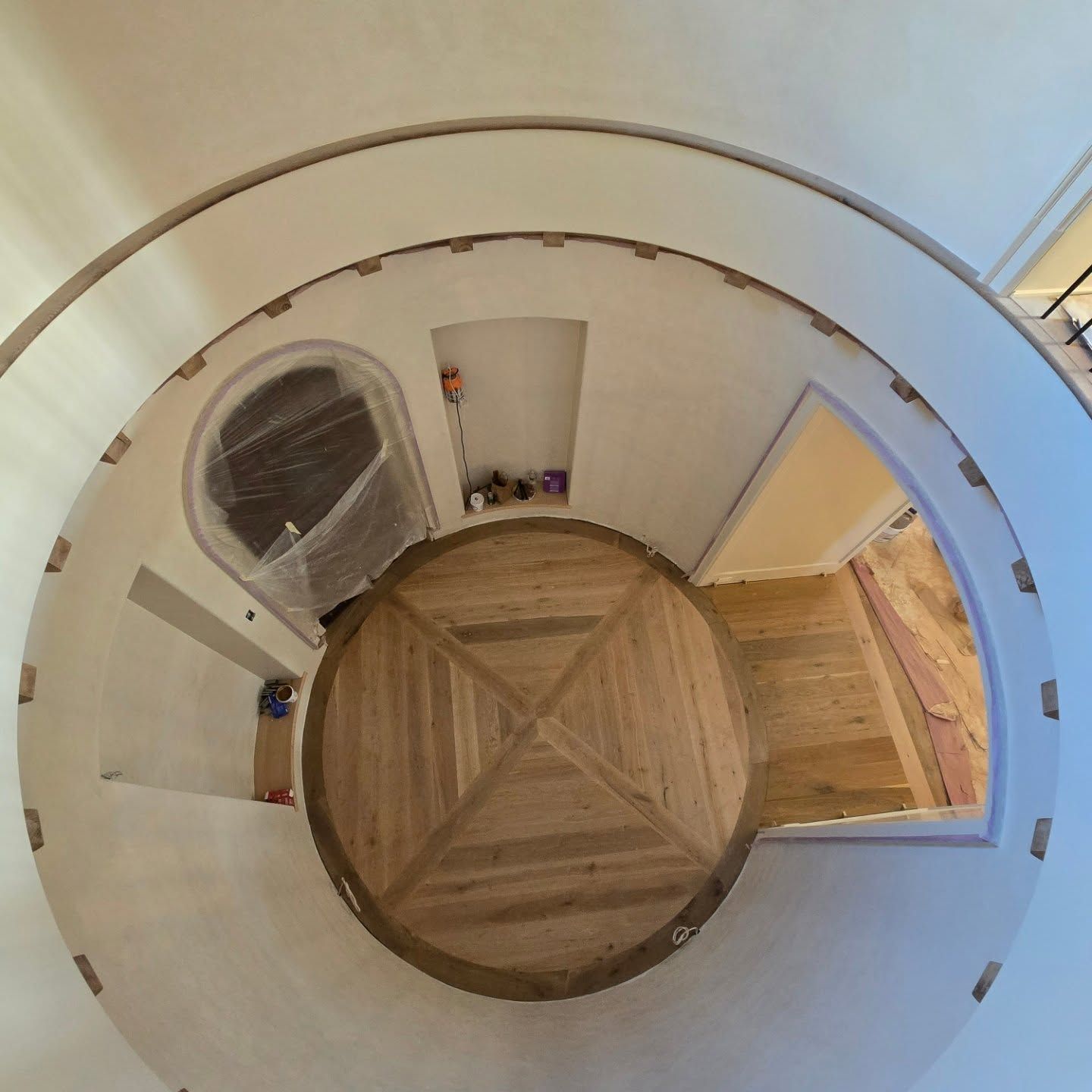 A high-angle view of a circular room under construction, showing finished hardwood flooring with a geometric pattern.