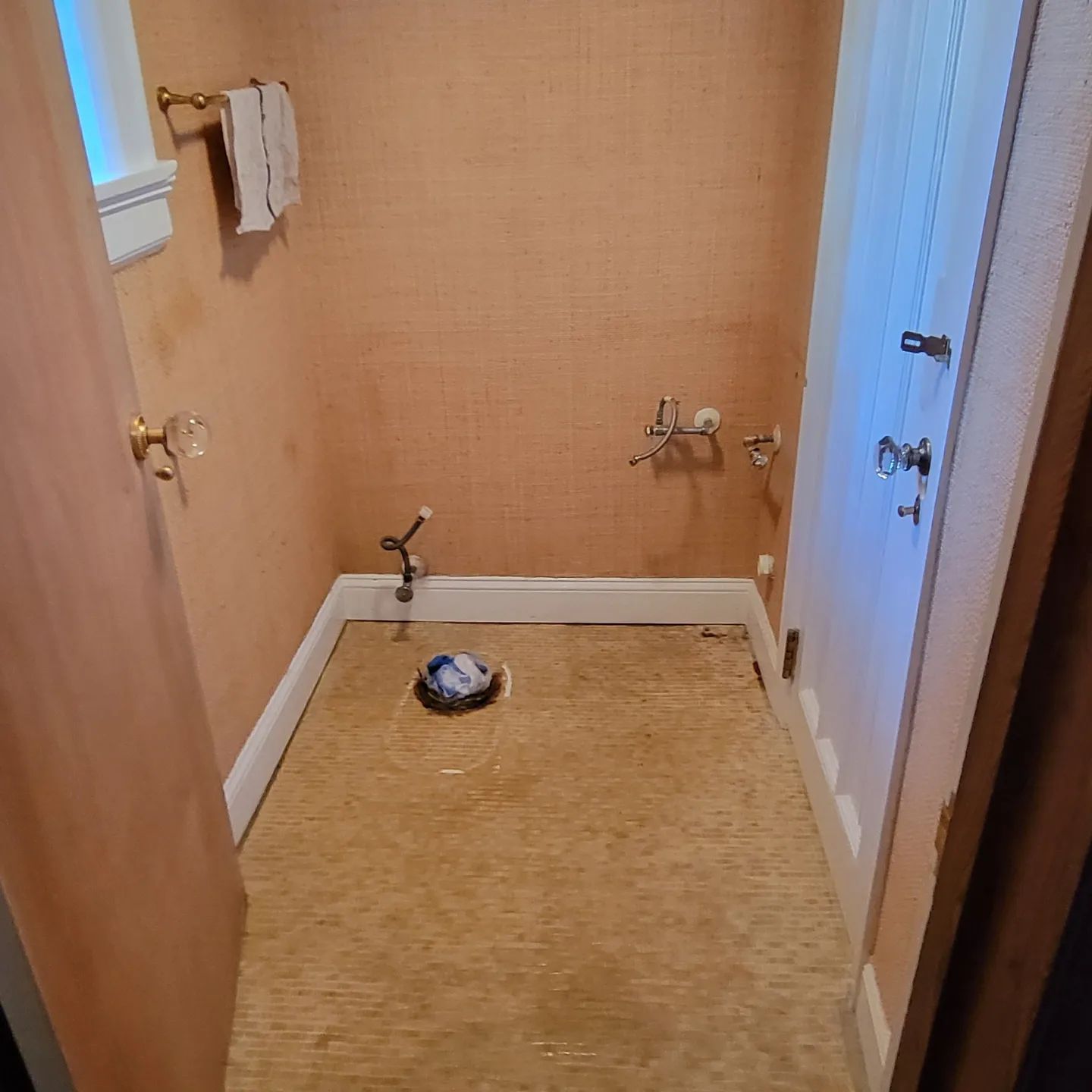 A small, empty bathroom undergoing renovation with orange walls, a toilet flange in the center, and plumbing fixtures.
