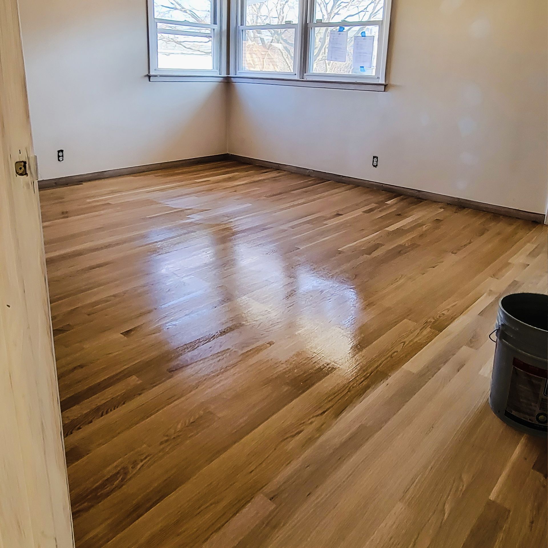 A partially finished hardwood floor in an empty room with natural light reflecting on the polished, golden wood.