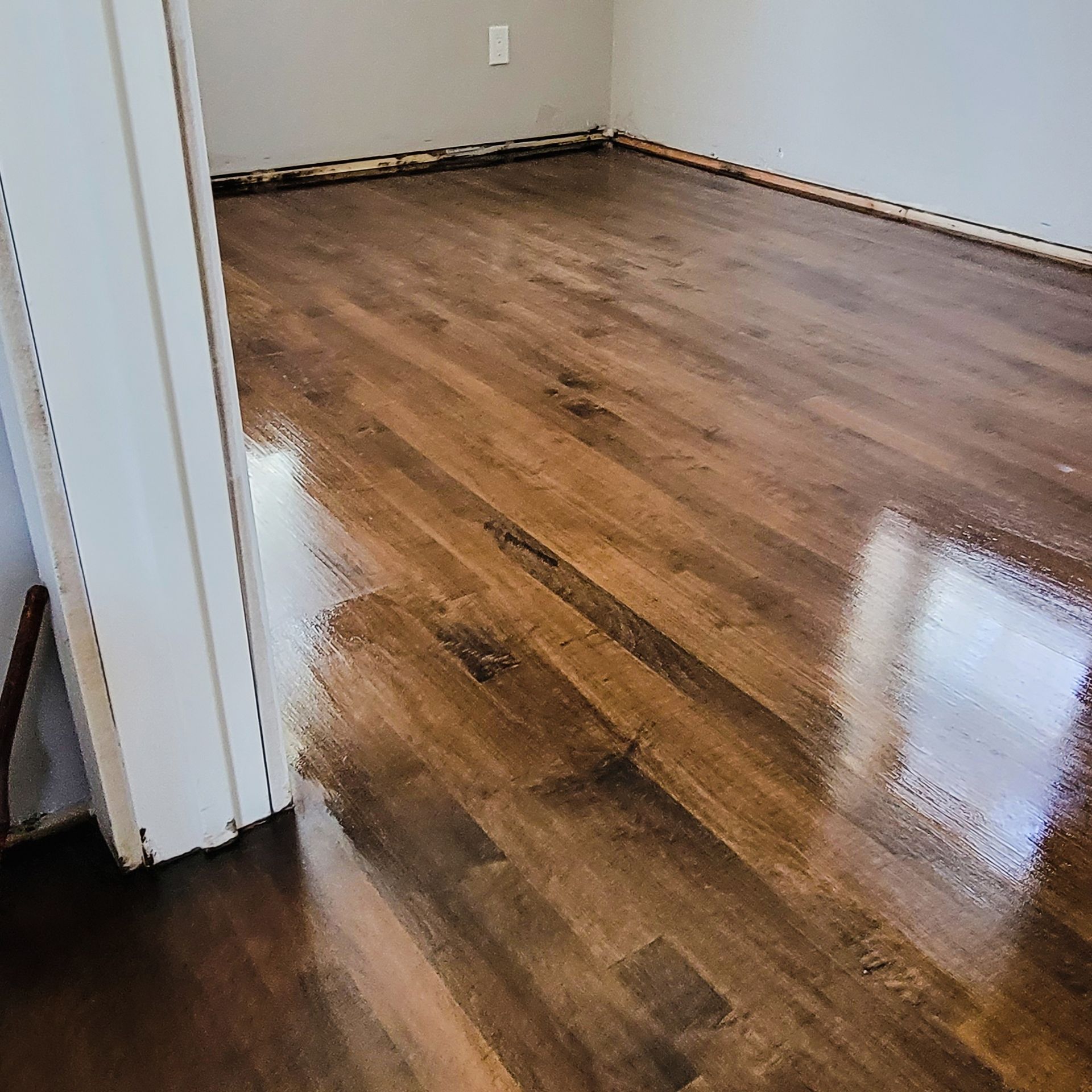 Newly installed dark-stained hardwood flooring in a room with light gray walls, showing a glossy finish and wood grain.