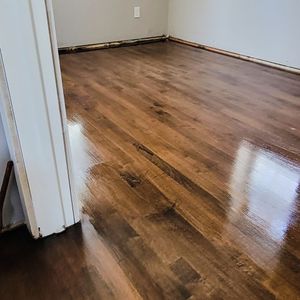 A room with dark, polished hardwood flooring and light-colored walls, featuring a doorway and an electrical outlet.