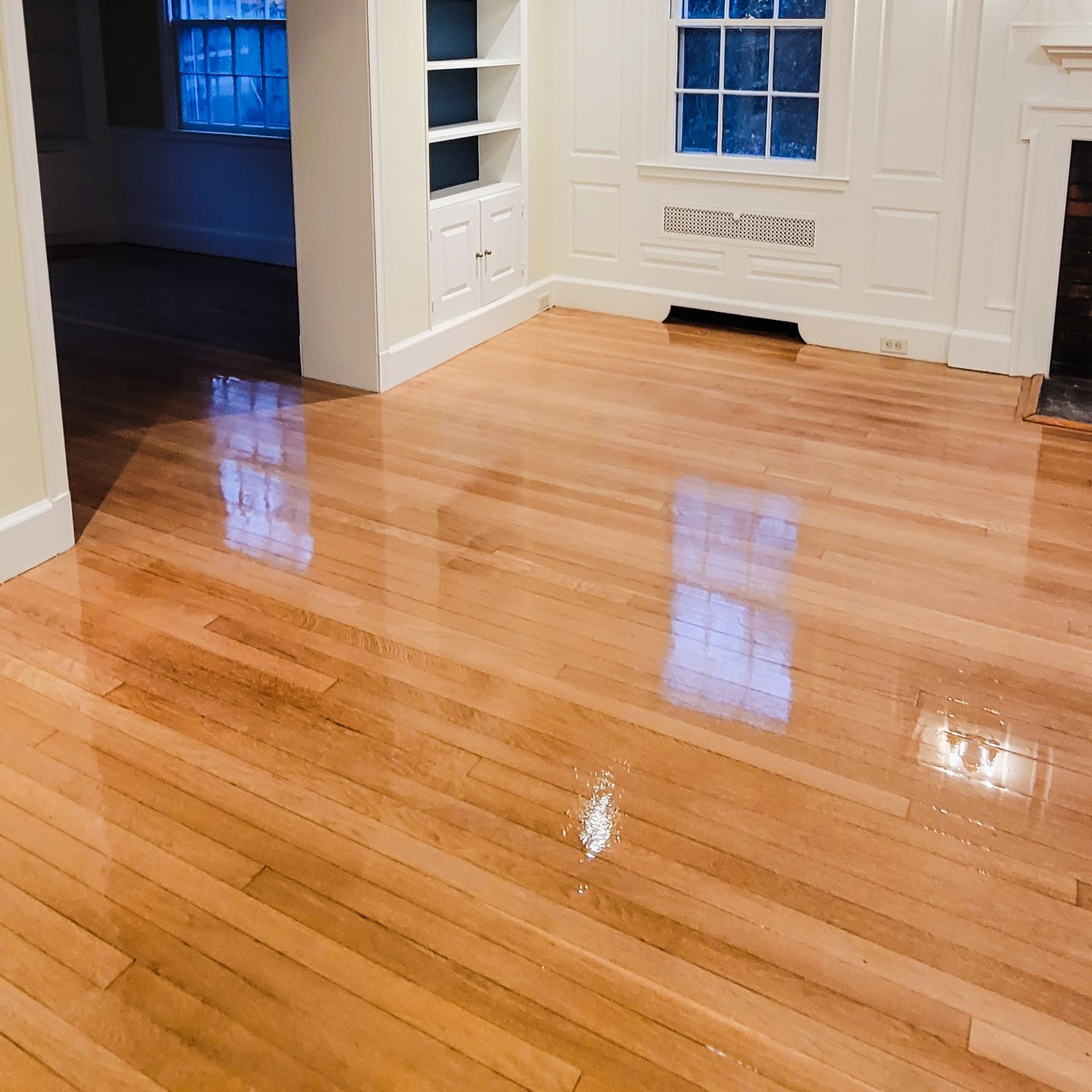 A bright, spacious room with polished light-wood hardwood floors, built-in shelving, a fireplace, and a window.