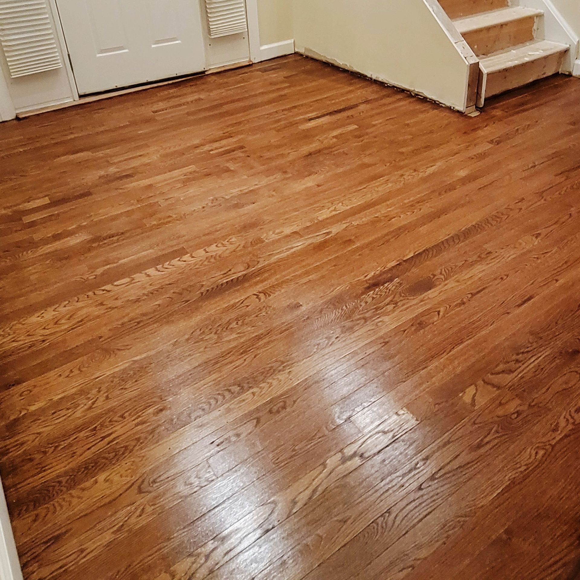 A high-angle view of a newly finished, warm-toned oak hardwood floor in a room with white trim and a staircase.