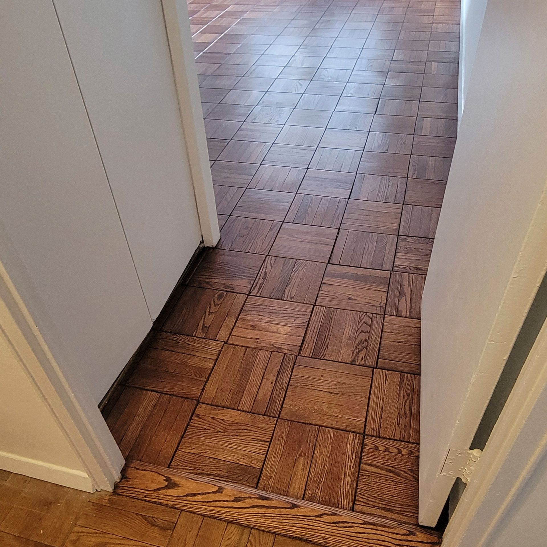 A doorway looking into a room with brown parquet wood flooring and a matching wooden floor transition strip.