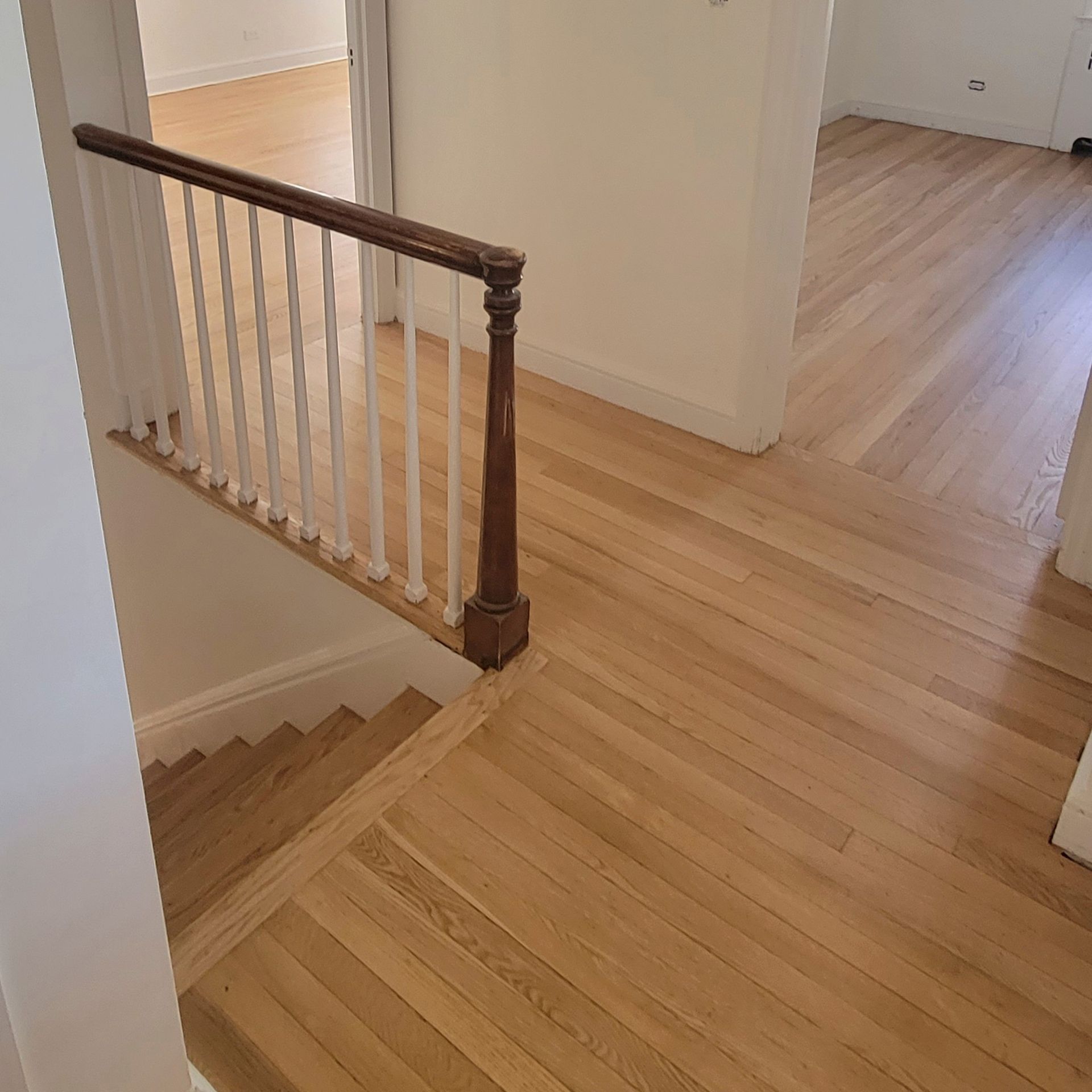 A view from above looking down a wooden staircase with a wooden railing and white spindles next to hardwood floor hallways.