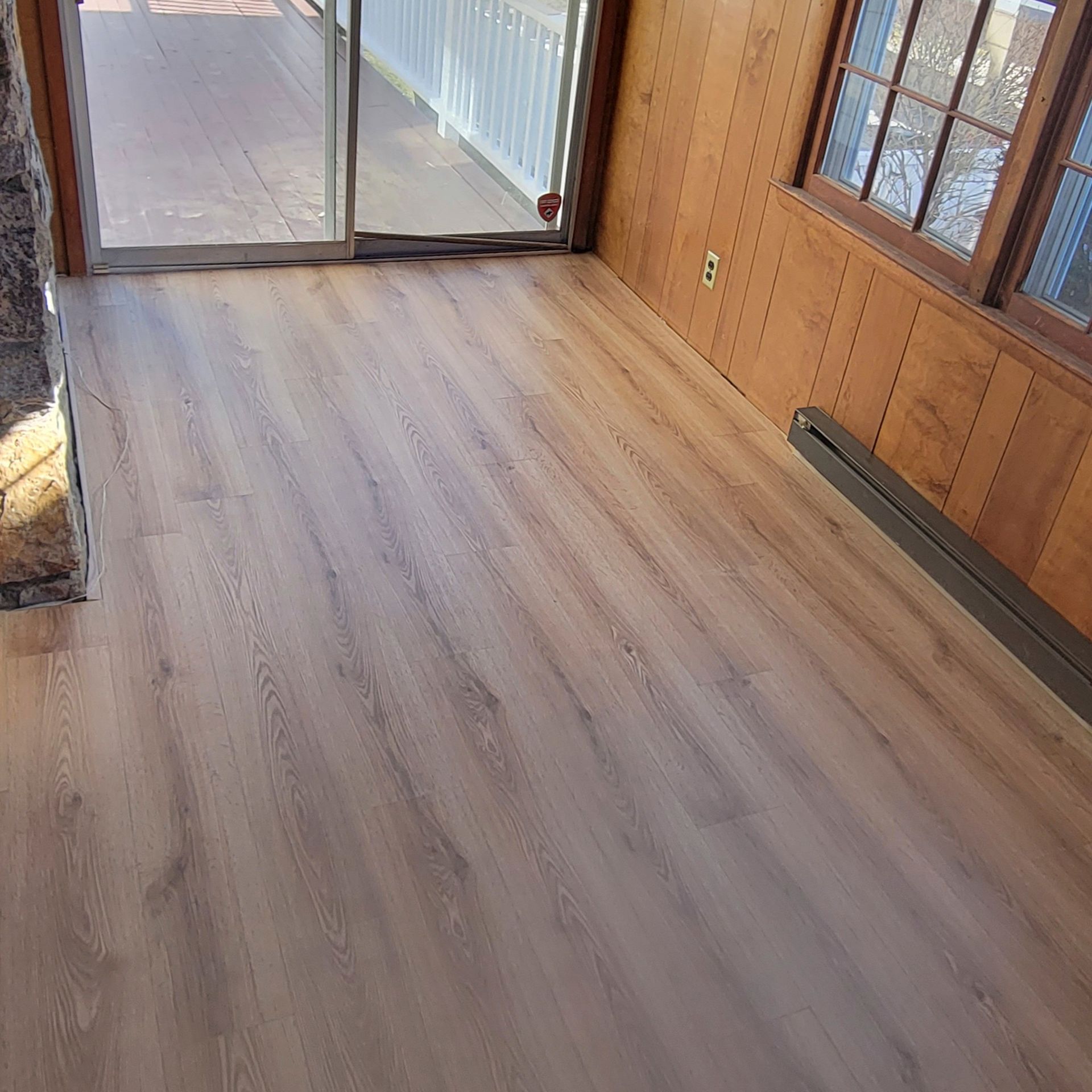 A room with light wood-look vinyl plank flooring, a glass sliding door, and wood-paneled walls.
