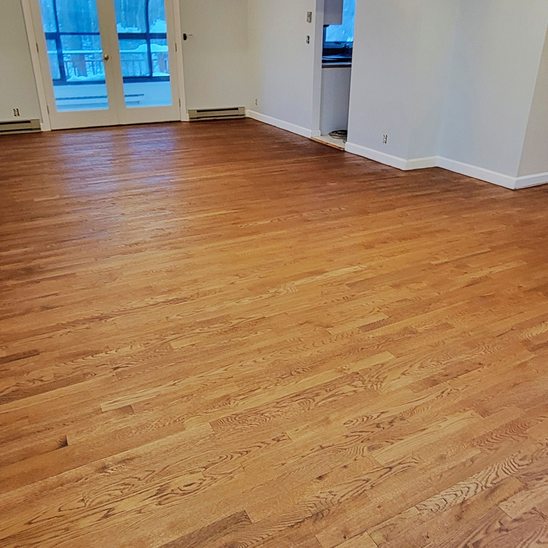 A bright, open room featuring polished light-brown hardwood flooring, white walls, white trim, and a glass sliding door.