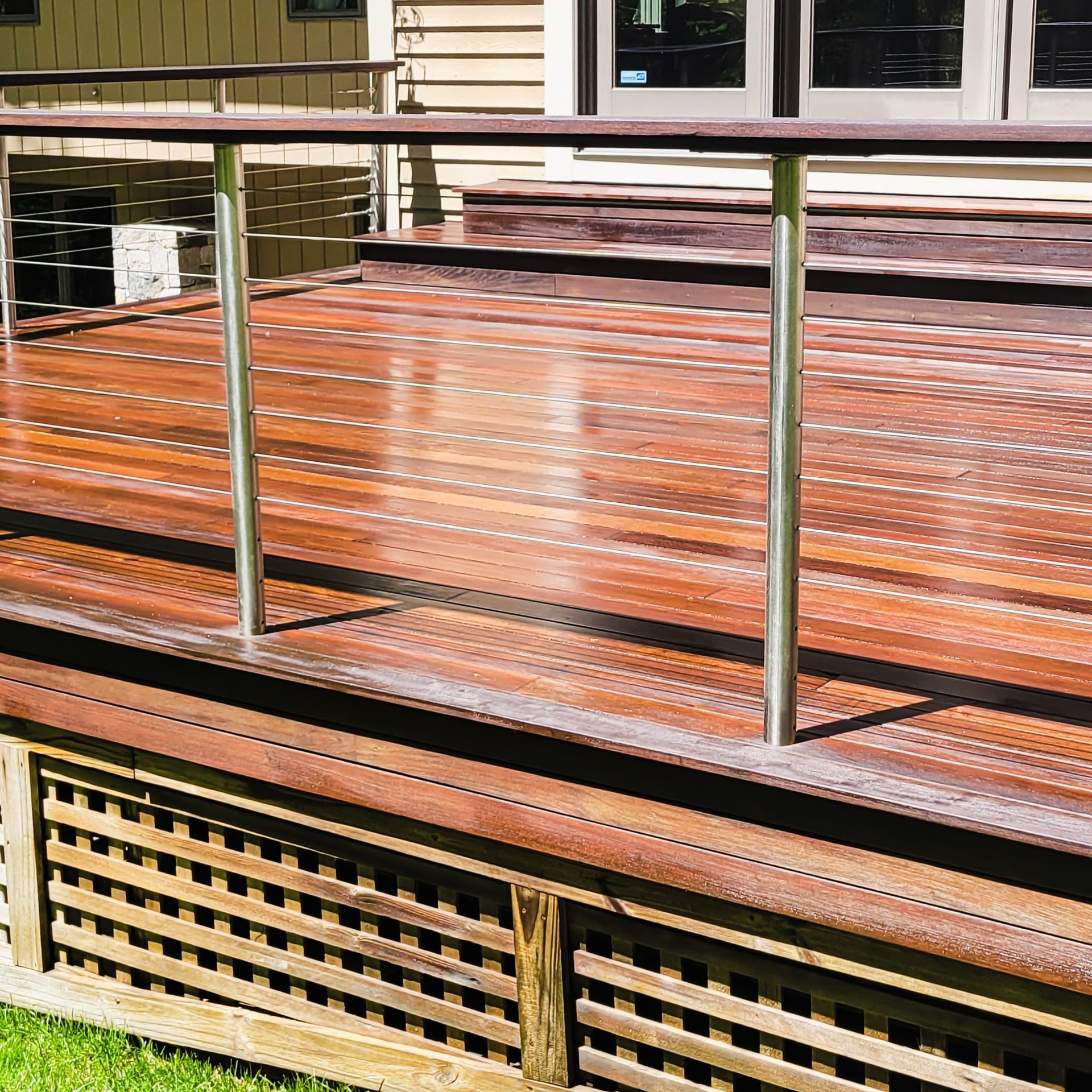 A wooden deck with a horizontal railing and lattice skirting, viewed from a slightly elevated angle.