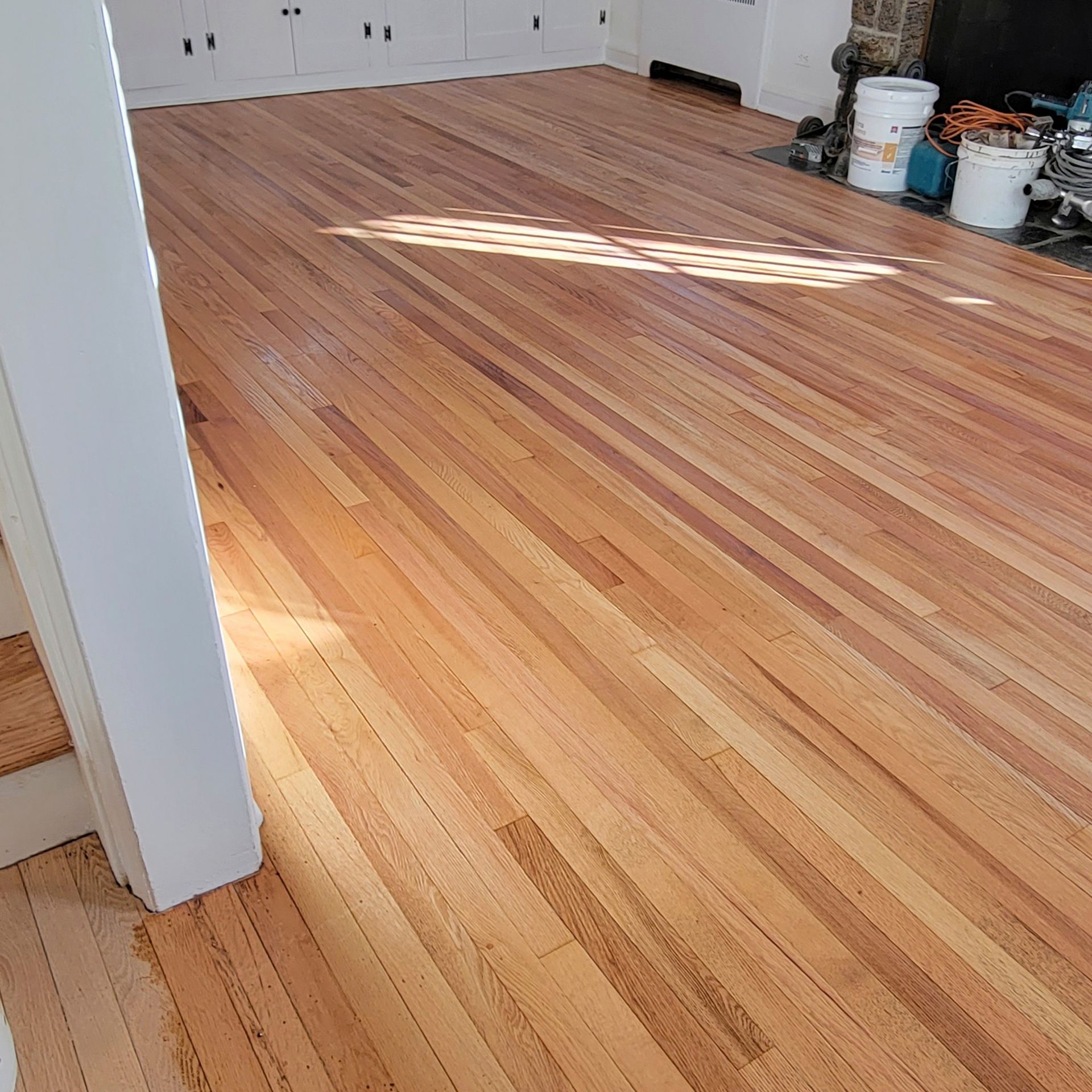 Newly sanded, light-colored hardwood flooring installed in a room with a white doorway and wall cabinets.