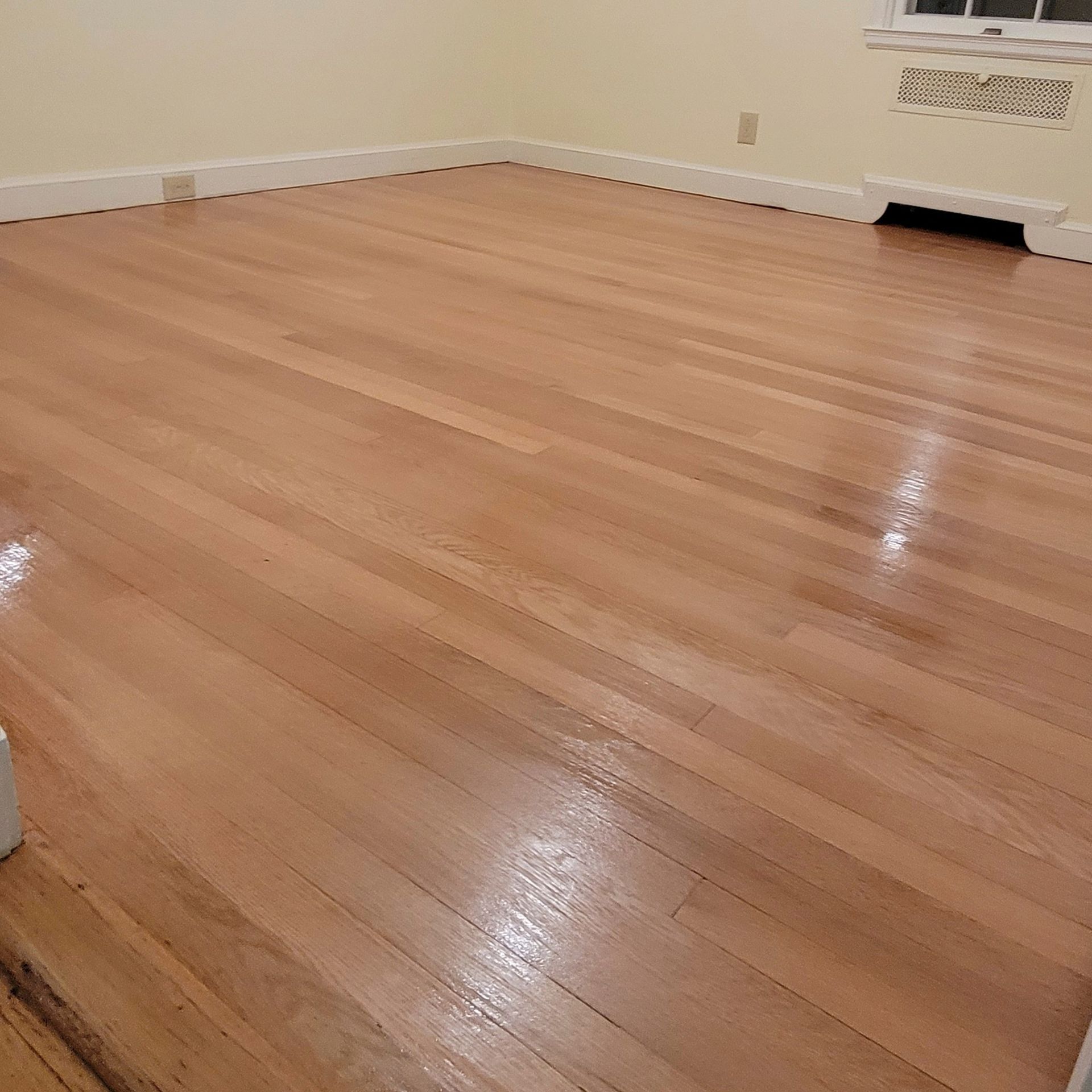 A high-angle view of a room with polished, light-colored hardwood flooring, white baseboards, and pale yellow walls.