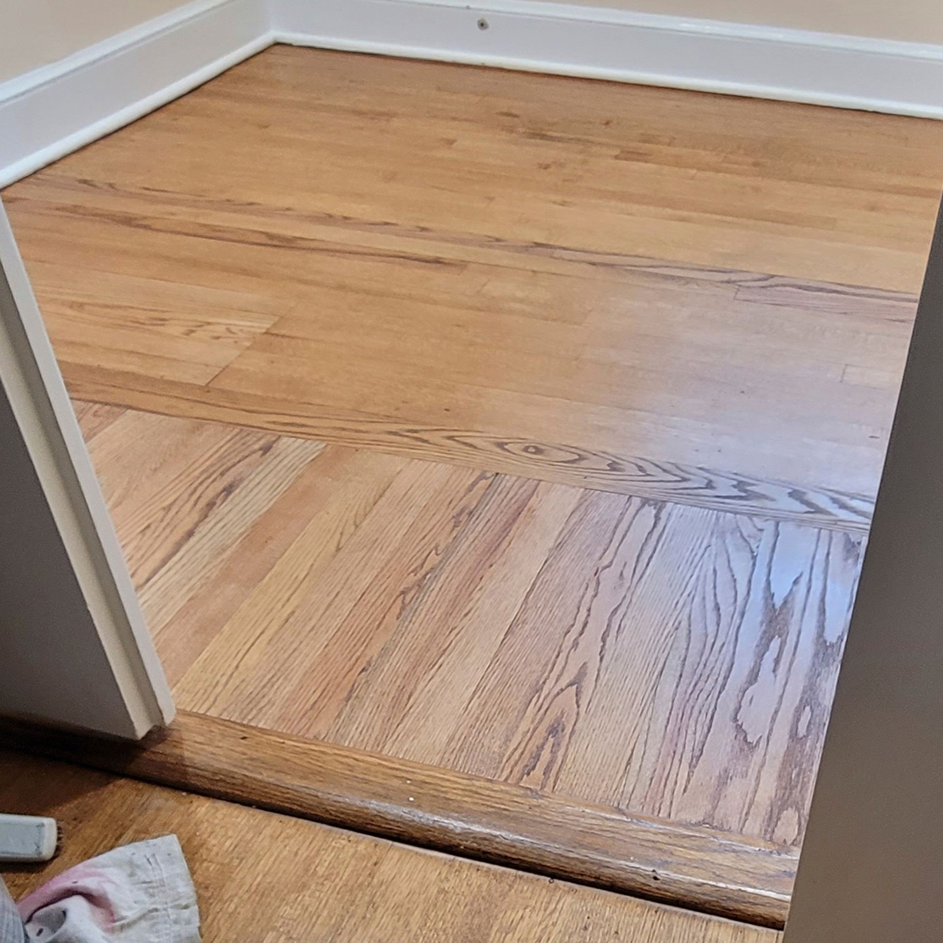 Light oak hardwood flooring with a transition threshold between two rooms of slightly different wood tones.