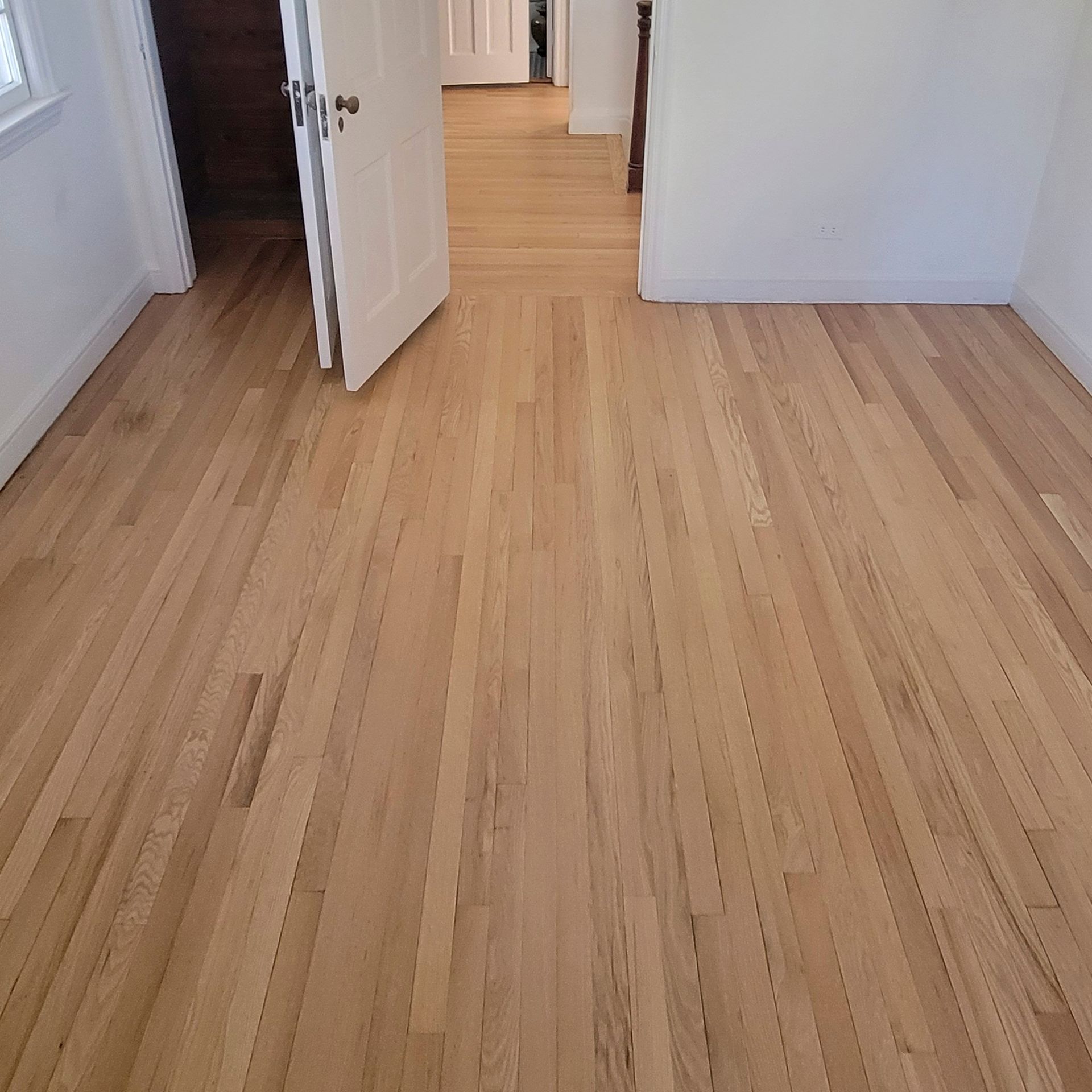 Newly finished, light-toned hardwood floors extend from an open doorway into a bright, white-walled room.