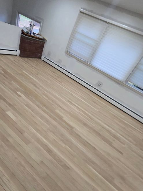 A room with light-colored wood flooring, white walls, white window blinds, and a brown cabinet in the corner.