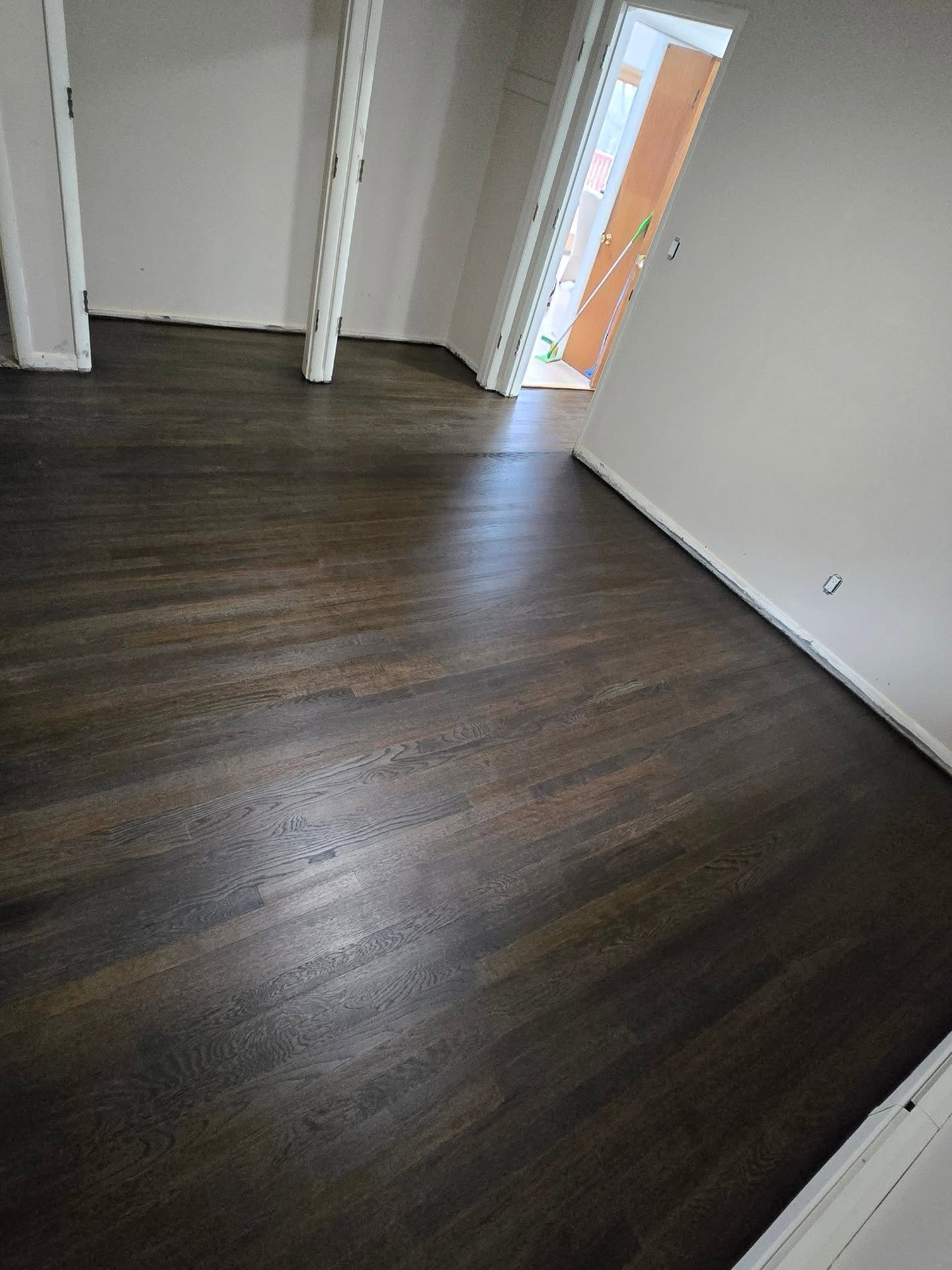 A room with dark-stained hardwood flooring and white walls, looking toward a doorway.