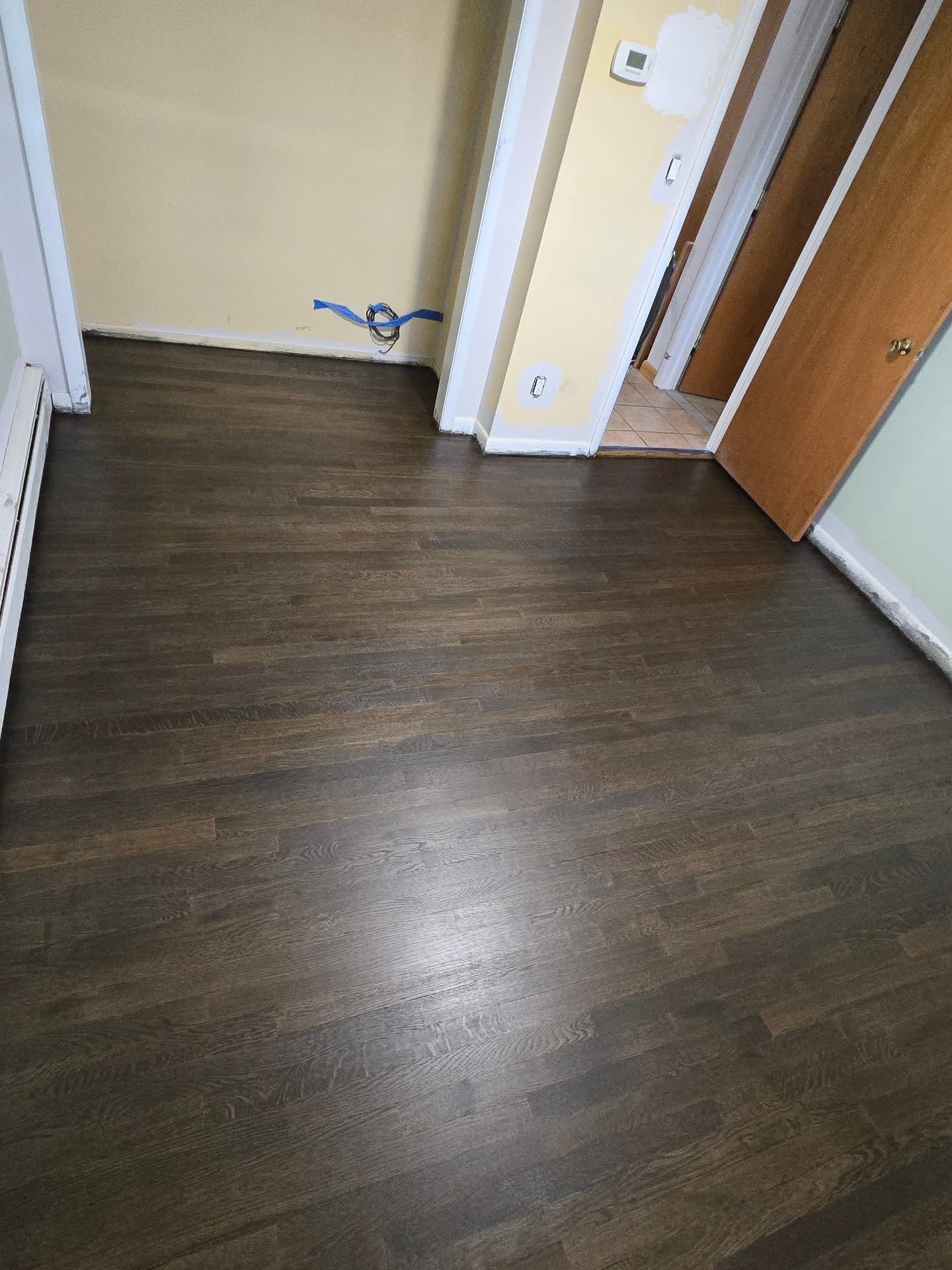 A room with dark stained wood flooring, light beige walls, and an open wooden door leading to another area.