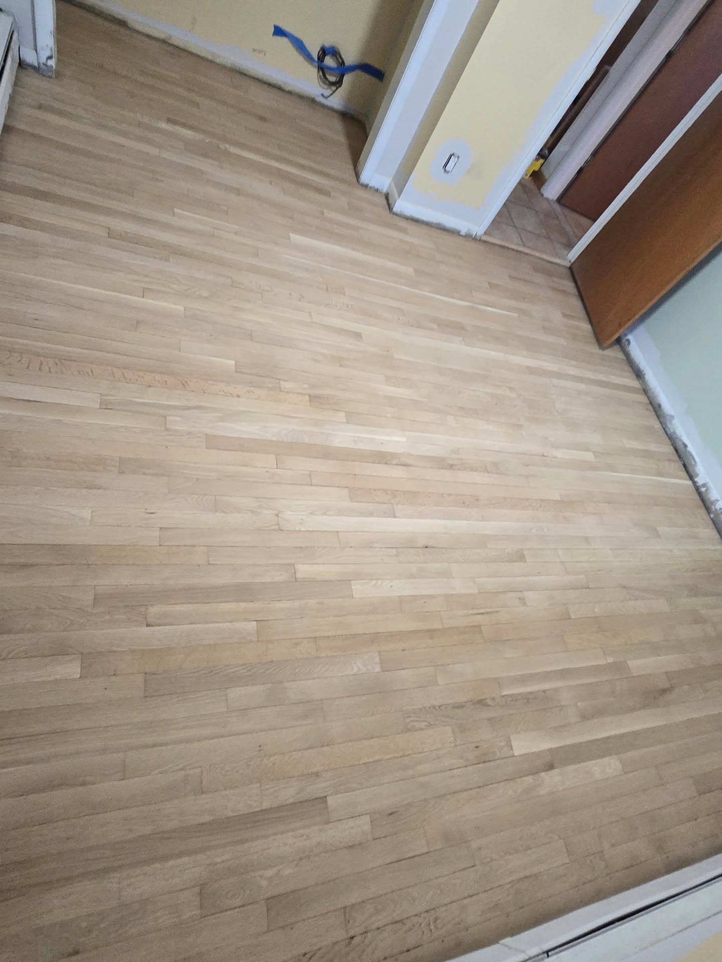A freshly sanded, light-colored hardwood floor in a room under renovation.