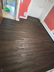 A room with freshly stained dark brown hardwood floors, pink-painted walls, and an open doorway leading to a tiled area.