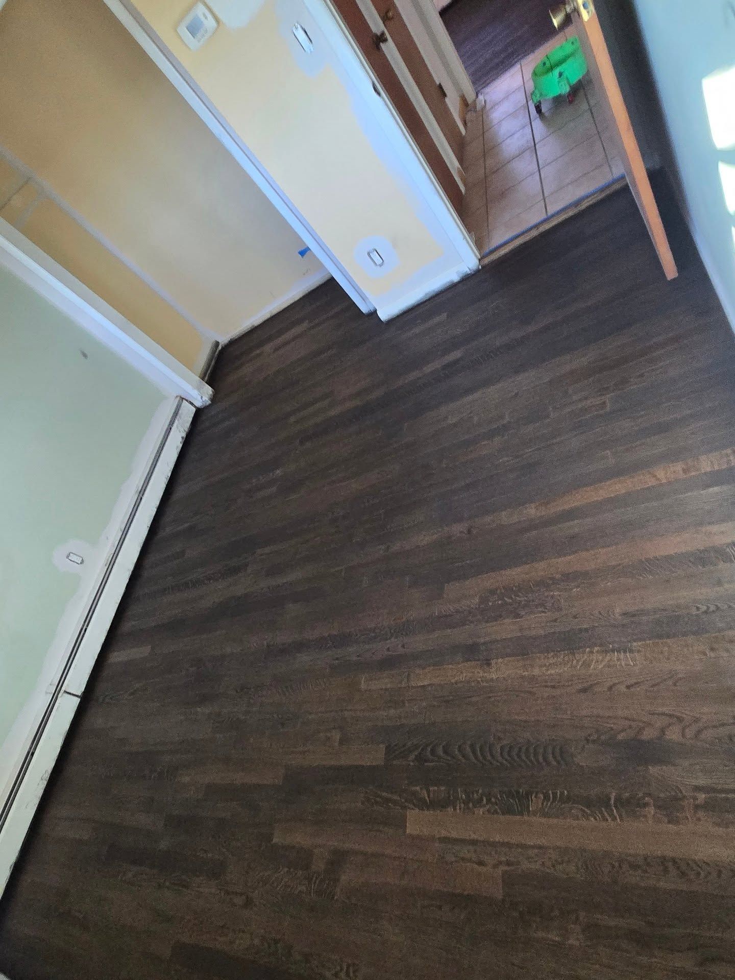A room with dark-stained hardwood floors, light yellow walls, and white trim, with a doorway leading to a tiled area.
