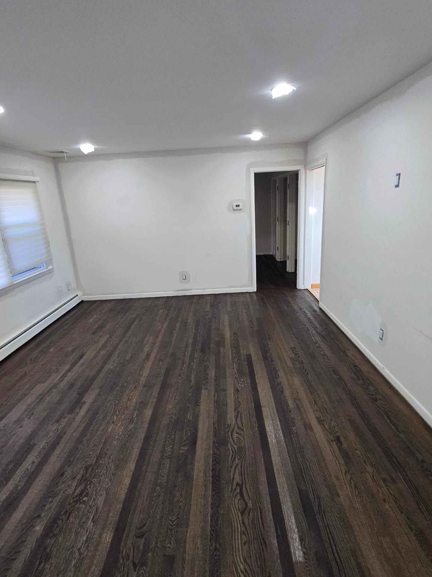 Empty room with dark wood-look laminate flooring, white walls, recessed ceiling lights, and an open doorway.