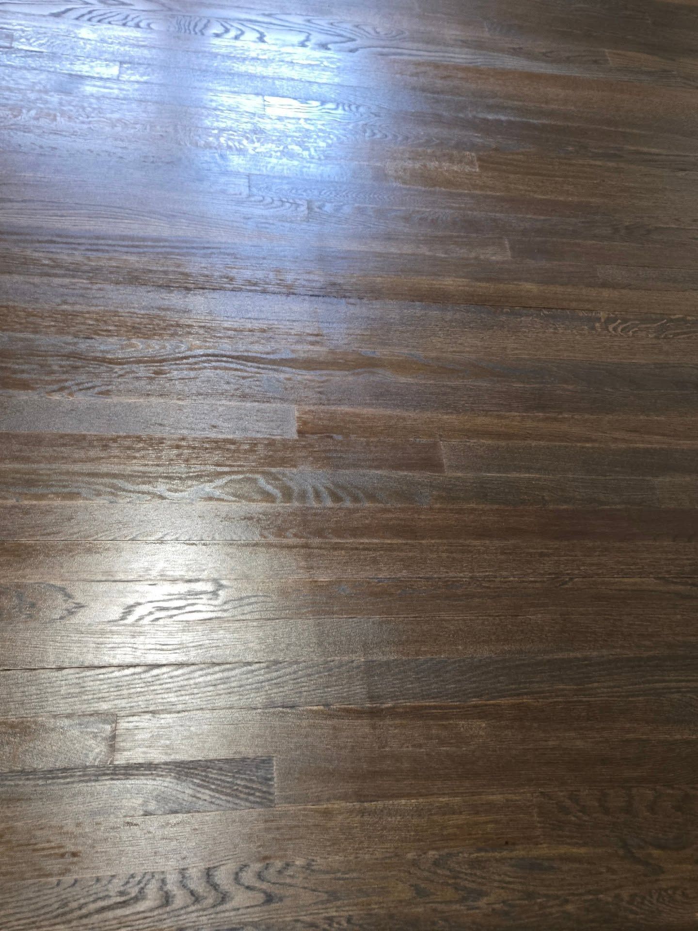 A close-up, high-angle view of brown stained hardwood floorboards with visible wood grain and light reflection.